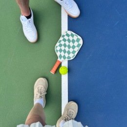 feet, a paddle and a pickleball on a pickleball court